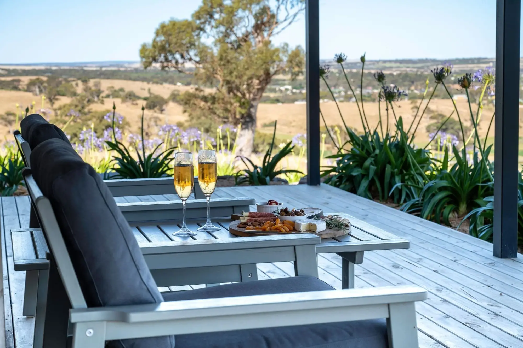 Two glasses of champagne and a platter on the deck table, the paddocks and the far ridge beyond the rail.